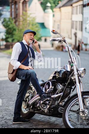 Un uomo d'affari senior con moto in città, utilizzando smartphone. Foto Stock