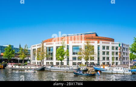 Amsterdam, 7 maggio 2018 - Vista sul fiume Amstel pieno di piccole barche e lo Stopera (edificio dell'opera) sullo sfondo di una giornata estiva Foto Stock