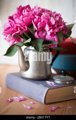 belle peonie rosa in una vecchia teiera in metallo per il tè in piedi su un libro. carta da parati per smartphone Foto Stock