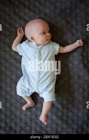 Un bambino neonato che si stesa su un tappeto scuro. Foto di Sam Mellish Foto Stock