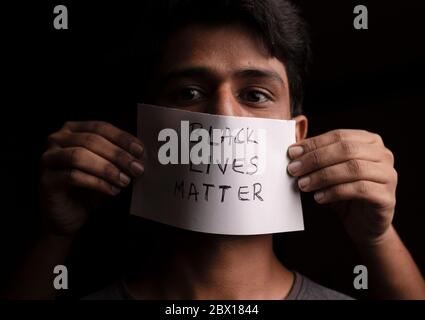 Il volto del giovane uomo coperto con poster di carta Black Lives Matter - concetto di discriminazione razziale contro i neri. Foto Stock