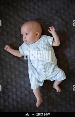 Un bambino neonato che si stesa su un tappeto scuro. Foto di Sam Mellish Foto Stock