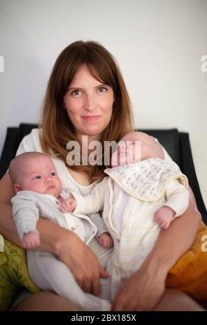 Una madre seduta giù guardando nella macchina fotografica con i gemelli neonati del ragazzo e della ragazza, Londra. Foto di Sam Mellish Foto Stock