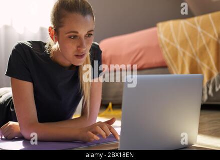 Giovane donna che partecipa a una lezione di fitness online di fronte al computer portatile. Foto Stock