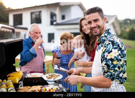 Ritratto di famiglia multigeneration all'aperto su barbecue giardino, grigliatura. Foto Stock