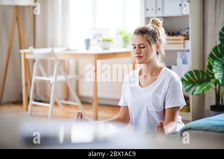 Giovane donna che fa l'esercitazione di yoga all'interno a casa, meditating. Foto Stock