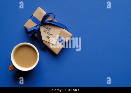 Confezione regalo vintage con iscrizione Happy Father's Day e tazza di caffè su sfondo blu. Disposizione piatta, vista dall'alto, spazio per la copia. Foto Stock