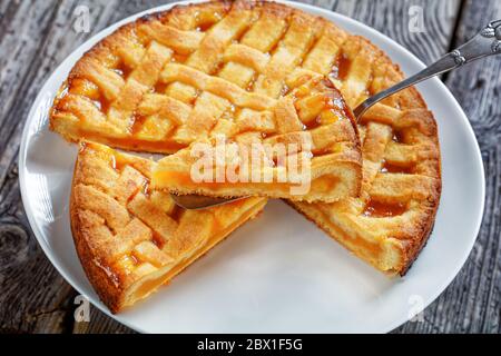 primo piano di torta di albicocche a fette con crosta di torta a graticcio che si stocca su una pala per torte vintage su un piatto bianco su un rustico tavolo di legno, paesaggista Foto Stock