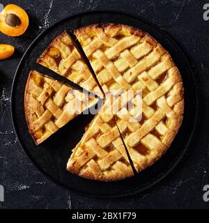 primo piano di torta di frolla di albicocca tagliata a fette con una crosta di torta di reticolo che si stocca su una piastra nera su un tavolo di cemento, piatto, spazio libero Foto Stock