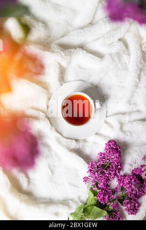 Tè nero caldo fresco in una bella tazza di porcellana con bouquet lilla, piatto, modello di sfondo Foto Stock