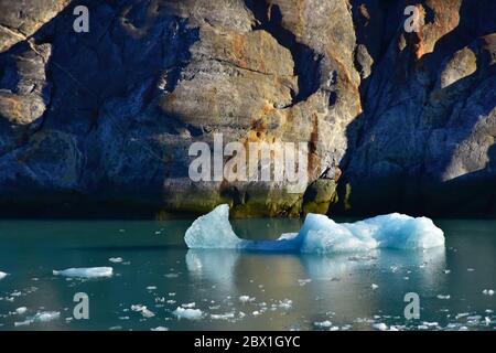 Un iceberg blu solato che galleggia sulle rocce ricoperte di licheni nel fiordo Tracy Arm, vicino a Juneau, Alaska. Foto Stock