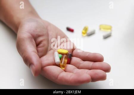 Vista dall'alto di pillole colorate, medicine in capsula e un bicchiere d'acqua nelle mani dell'uomo. Trattamento di COVID-19 a casa secondo le raccomandazioni del medico. Foto Stock