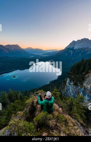 Donna che guarda sul lago Eibsee e sul massiccio di Zugspitze con Zugspitze, alba, catena montuosa di Wetterstein, vicino a Grainau, alta Baviera, Baviera, Germania Foto Stock