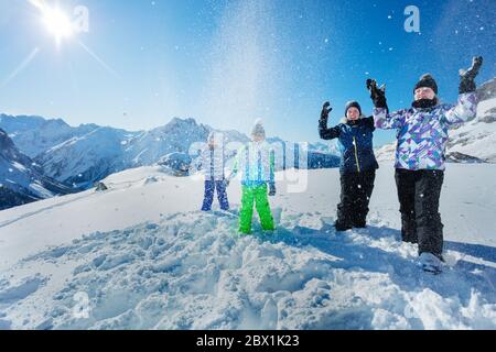 Un grande gruppo di bambini si diverte a gettare la neve nell'aria sopra una splendida vista sulle montagne Foto Stock