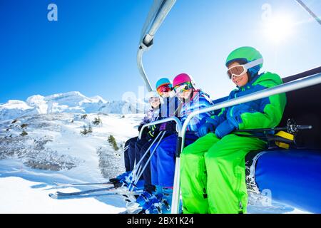 Ritratto a vista bassa di quattro bambini felici in vivido attrezzatura da sci che si solleva sulla seggiovia sulla montagna insieme e sorridendo Foto Stock