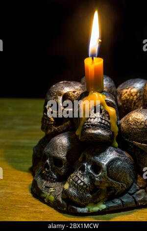 teschi con candela che brucia su sfondo di legno nel buio Foto Stock