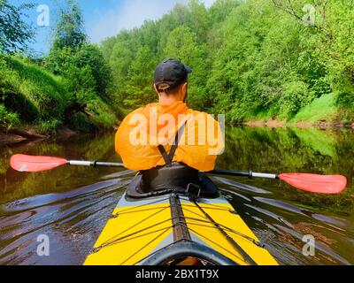 Gli uomini in un cappello e impermeabile di colore arancio galleggia su un kayak sulla foresta fiume tranquillo, il bellissimo paesaggio, un tempo mutevole, attivamente Foto Stock