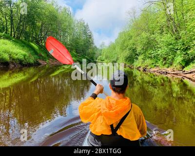 Gli uomini in un cappello e impermeabile di colore arancio galleggia su un kayak sulla foresta fiume tranquillo, il bellissimo paesaggio, un tempo mutevole, attivamente Foto Stock