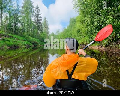 Gli uomini in un cappello e impermeabile di colore arancio galleggia su un kayak sulla foresta fiume tranquillo, il bellissimo paesaggio, un tempo mutevole, attivamente Foto Stock