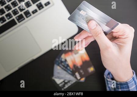 Maschio di mani tenendo la carta di credito, computer portatile sul tavolo, shopping online concetto. Foto Stock