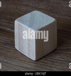 Un blocco o cubo di legno liscio che mostra tre lati vuoti su uno sfondo di legno con contrasto elevato e spazio di copia Foto Stock