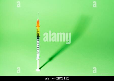 Siringa per vaccino o insulina, con la sua ombra, su sfondo verde. Concetti di salute, vaccinazione, coronarivus o farmaci Foto Stock