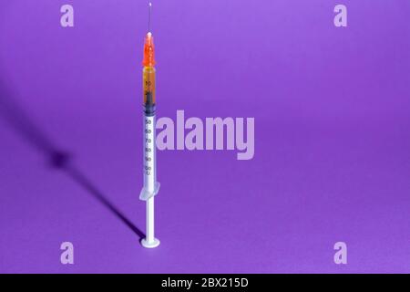 Siringa per vaccino o insulina, con la sua ombra, su sfondo viola. Concetti di salute, vaccinazione, coronarivus o farmaci Foto Stock