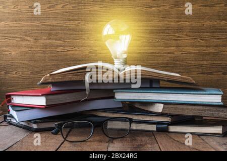 Apri libro con lampadina, libri e bicchieri su tavolo di legno. Foto Stock