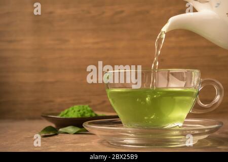 Il tè verde viene versato in una tazza di tè di vetro sul tavolo Foto Stock