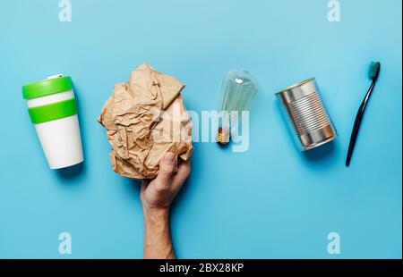 Riciclaggio e riutilizzo delle risorse. Concetto ecologico. Oggetti su sfondo blu: Vetro di plastica, carta, metallo, vetro, mano umana. Foto Stock