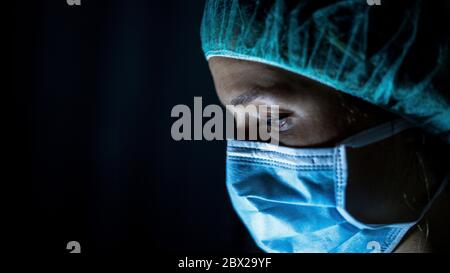 Ritratto di giovane chirurgo, indossando una maschera chirurgica, davanti a sfondo nero Foto Stock