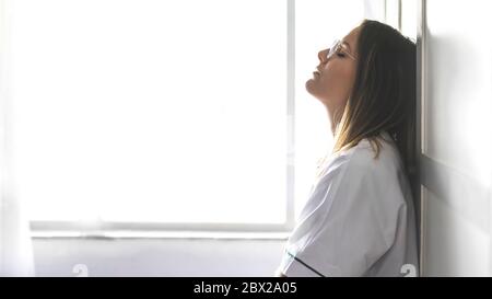 Infermiera stanca appoggiata a parete nel corridoio dell'ospedale Foto Stock