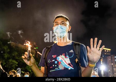 Un partecipante ha tenuto una candela su una mano, E tenne cinque dita per segnalare le "5 richieste" del movimento pro-democrazia di Hong Kong durante la veglia commemorativa a Victoria Park. Migliaia di persone si sono riunite per la veglia commemorativa annuale a Victoria Park per celebrare il massacro di Piazza Tiananmen del 1989 nonostante un divieto della polizia che cita il coronavirus restrizioni di allontanamento sociale. Foto Stock