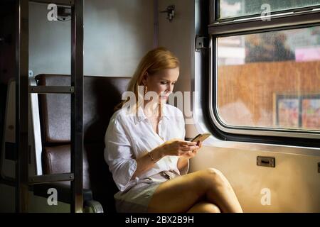 Una donna che usa uno smartphone su un treno Foto Stock
