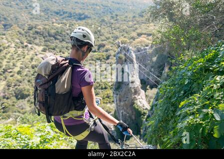 Concetto: Avventura. Donna con casco, imbracatura e zaino. Discesa in montagna da una via ferrata. Foto Stock