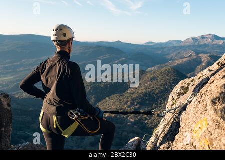 Concetto: Avventura. Donna arrampicatrice con casco e imbracatura. Dal retro si guarda al paesaggio naturale dell'Andalusia. Fissato alla parete naturale wi Foto Stock
