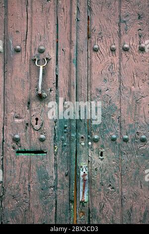 Vecchia porta rustica in legno con diversi strati di vernice spaccata nei colori rosa e verde Foto Stock