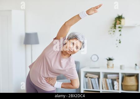Ritratto di donna anziana in abbigliamento sportivo facendo esercizi nel soggiorno a casa Foto Stock