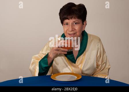 donna di 80 anni che beve un succo di pomodoro. Foto Stock