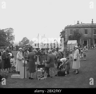 Anni '50, storici, adulti e bambini sui prati in un tradizionale inglese Country House Garden party o fete, con alcune madri bambini snd in fila per giocare una partita, Inghilterra, Regno Unito. Forse il periodo di massimo splendore del 'fete', era in questa epoca in cui una grande casa di campagna del villaggio che si abbona ad un proprietario di terra locale o squire avrebbe tenuta nei terreni una festa giardino per la gente locale di venire insieme raccogliere fondi per buone cause nella loro comunità. Foto Stock