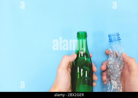 Mani che tengono il flacone vuoto di plastica e vetro su sfondo blu. Go Green Concept. Contenitore in vetro e plastica. Foto Stock