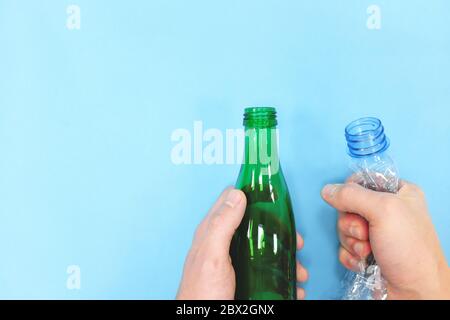 Mani che tengono il flacone vuoto di plastica e vetro su sfondo blu. Go Green Concept. Contenitore in vetro e plastica. Foto Stock