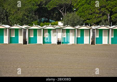 Fila di colorate capanne sulla spiaggia di sabbia con alberi sullo sfondo Foto Stock