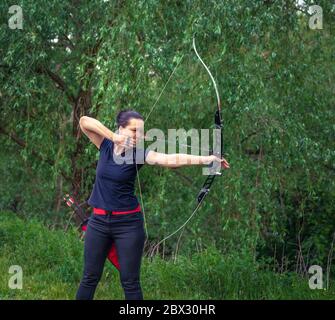 tiro con l'arco in natura. Una giovane donna attraente si sta allenando in un tiro di prua con una freccia a un bersaglio nei boschi Foto Stock