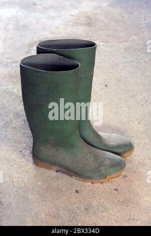 Vecchio paio di stivali Green Wellington (Wellies) indossati su un pavimento in cemento Foto Stock