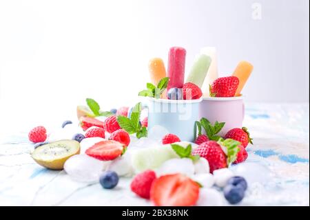 Papicle di frutta intera sane con fragole di Berries Kiwi su sfondo chiaro con un decor di ghiaccio, menta. Gustoso gelato alla frutta nella tazza. Spazio di copia. Foto Stock
