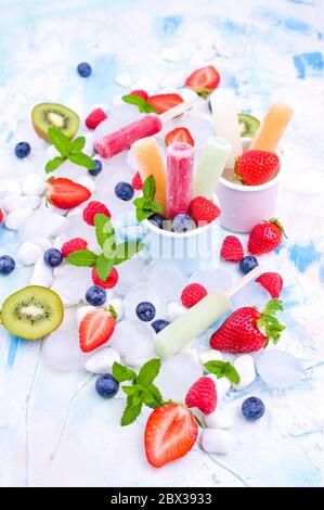 Papicle di frutta intera sane con fragole di Berries Kiwi su sfondo chiaro con un decor di ghiaccio, menta. Gustoso gelato alla frutta nella tazza. Spazio di copia. Foto Stock