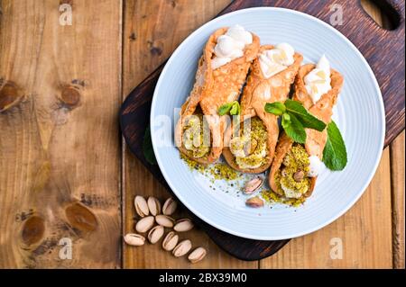 Cannoli Sicilia. Dolce tradizionale italiano con ricotta e ripieni vari. Cibo su un tagliere di legno Foto Stock