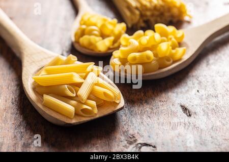 Vari tipi di pasta italiana cruda in cucchiai di legno su tavola di legno. Foto Stock