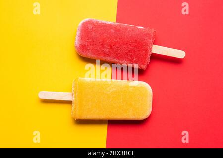 Due gelato di papsicle su sfondo giallo e rosso, sopra la vista. Piatto con ricecream fatto in casa da frutta Foto Stock